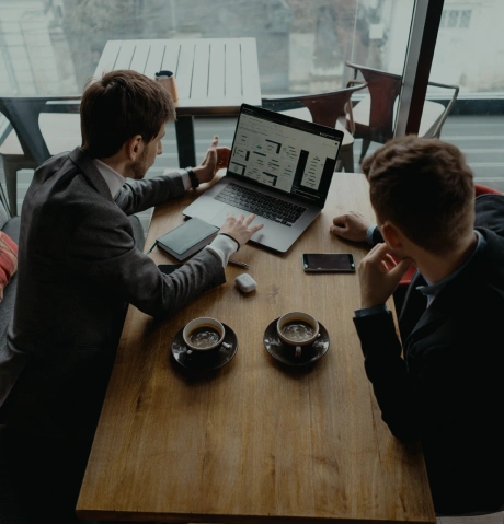 Two people working on a laptop together at a table with coffee cups in a cafe setting